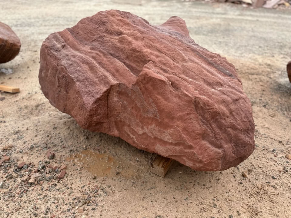 A large, reddish-brown rock with visible striations, resting on sandy ground.
