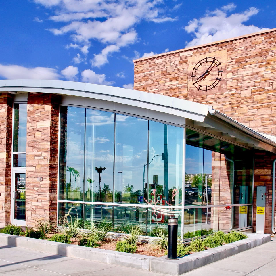 A modern building with large glass windows and a brick facade, featuring a curved roof and a small landscaped area in front.