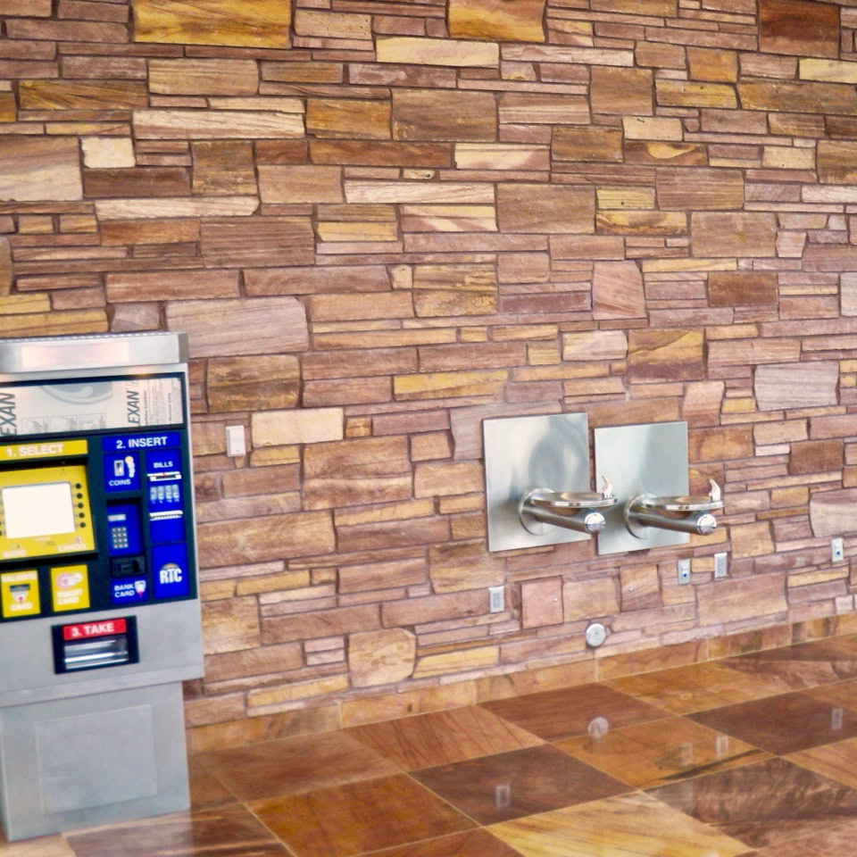 Vending machine and water fountains against a stone wall.