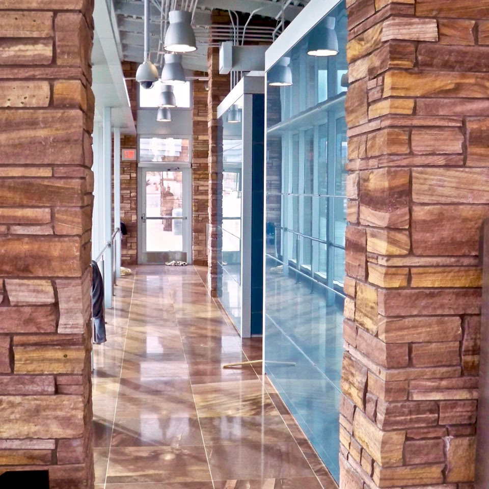 A hallway with polished stone walls and floor, featuring large windows and overhead lighting.