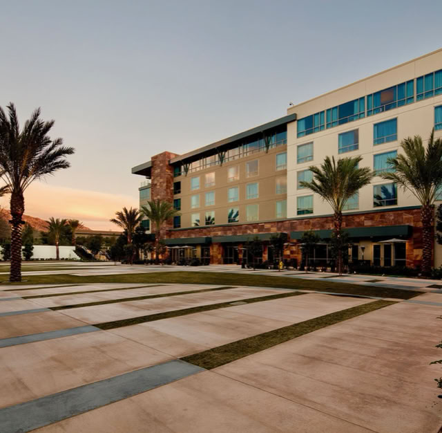 A modern multi-story building with large windows, surrounded by palm trees and a paved walkway, under a clear sky at sunset. AT THE viejas casino,CA.