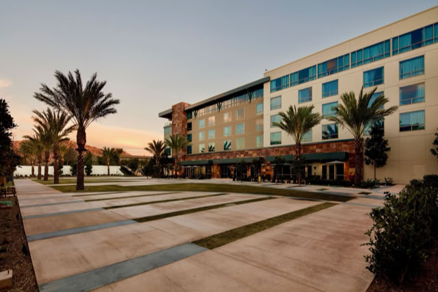 A modern multi-story building with large windows, surrounded by palm trees and a paved walkway, under a clear sky at sunset. AT THE viejas casino,CA.