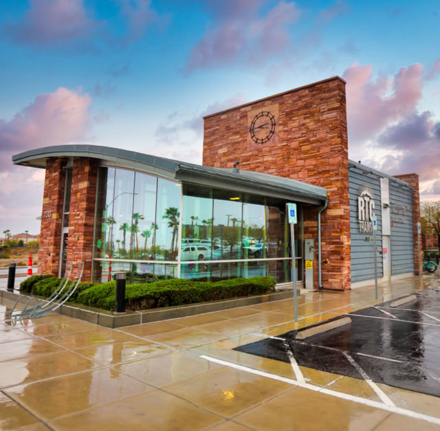 A modern building with large glass windows and a Stone facade, surrounded by a wet pavement and a cloudy sky. RTC BUS STOP .