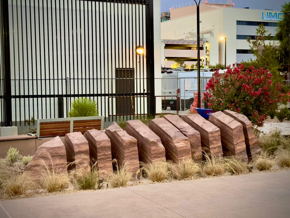 A row of large, sliced boulder arranged in a zigzag pattern, surrounded by dry grass, with a metal fence in the background. Located in Las Vegas, Nevada at the UNC trauma center by the emergency entrance