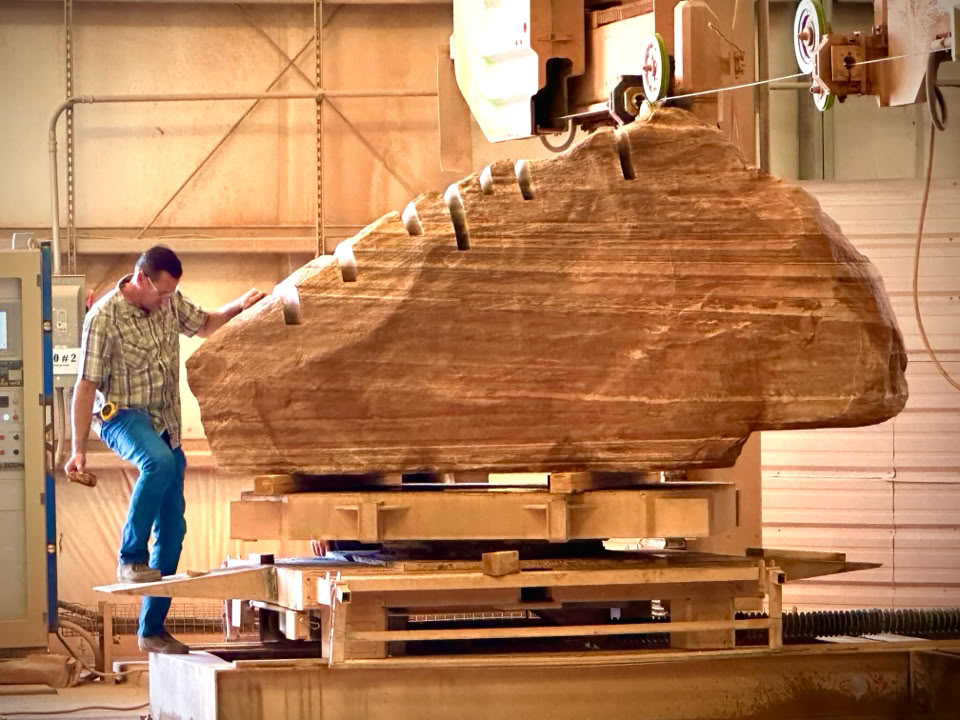 A person standing next to a large Stone Boulder , inside a workshop with machinery.