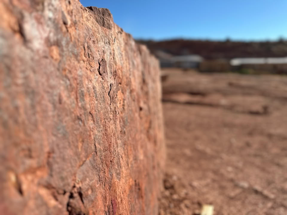 Close-up of a textured, reddish-brown Stone surface with a blurred background of an arid landscape and a clear blue sky.
