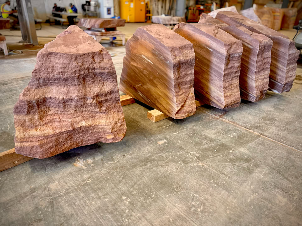 Large, rough-cut stone blocks with horizontal stripes, arranged in a row on a concrete floor.