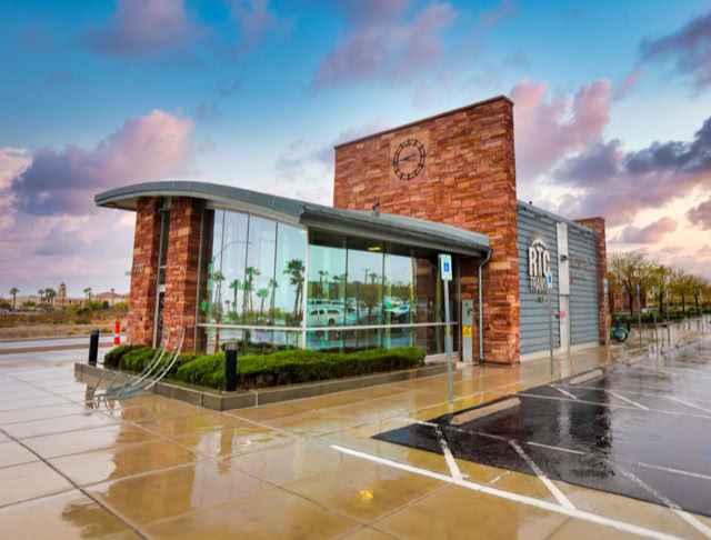 A modern building with large glass windows and a Stone facade, surrounded by a wet pavement and a cloudy sky. RTC BUS STOP .