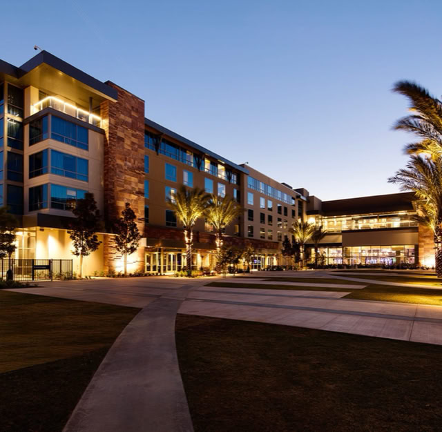 A modern multi-story building with large windows, surrounded by palm trees and illuminated at dusk. at Viejas Casino