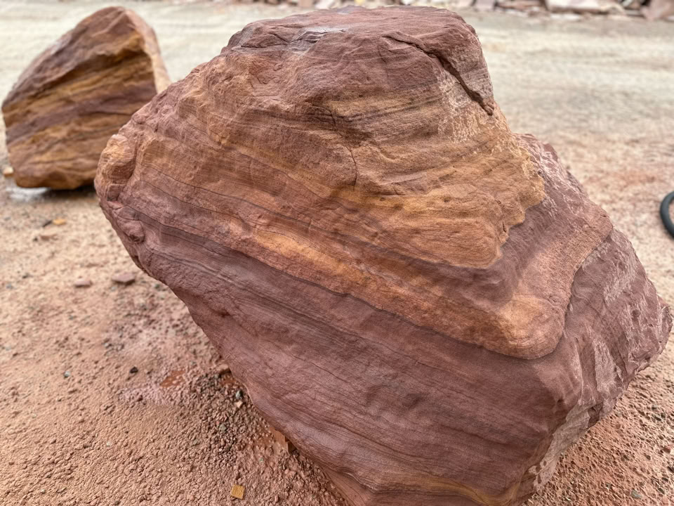A large, reddish-brown Stone with visible layers and rough texture, placed on sandy ground.
