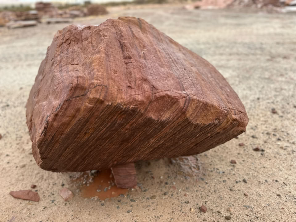 A large, reddish-brown rock with visible striations, resting on a sandy surface.