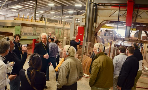 A group of people standing and talking inside a large industrial workshop with machinery and stone materials in the background.